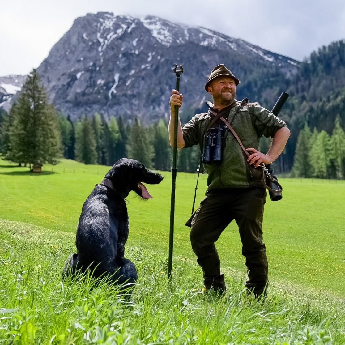 Jäger mit seinem Jagdstock und Jagdhund vor Bergkulisse